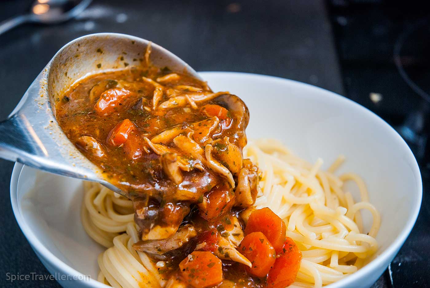 Ladling chicken wings pasta sauce over cooked spaghetti.