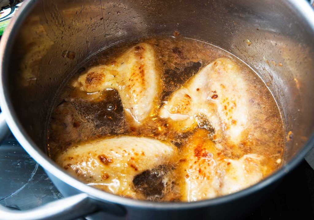 Chicken wings simmering in broth with onions and mushrooms in a large pot.