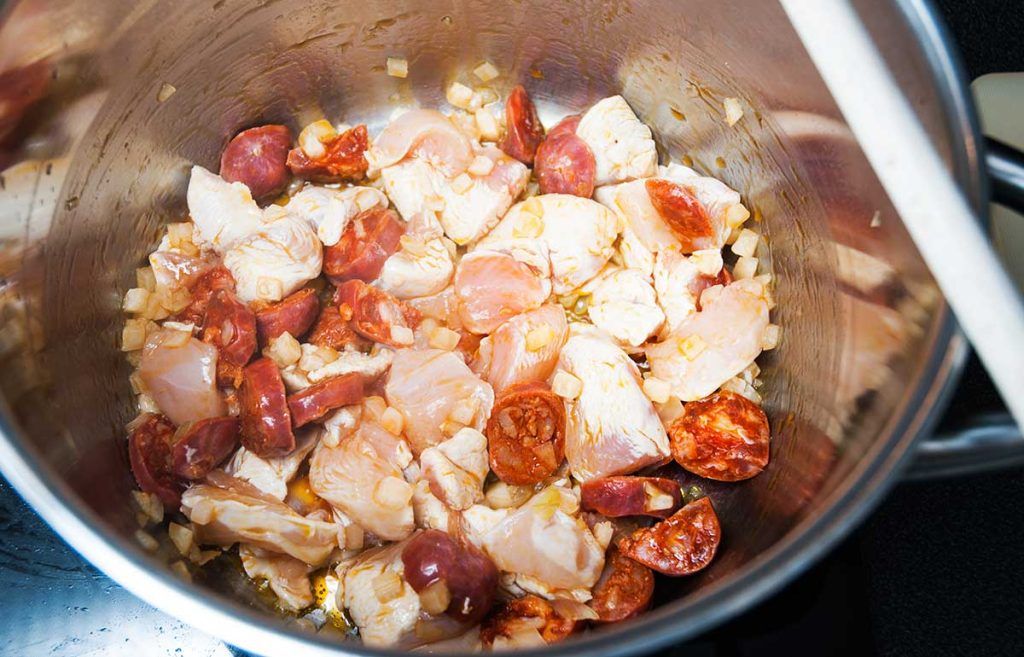 Chicken, onion, and chorizo frying together in a pot, with the chorizo releasing its oil.