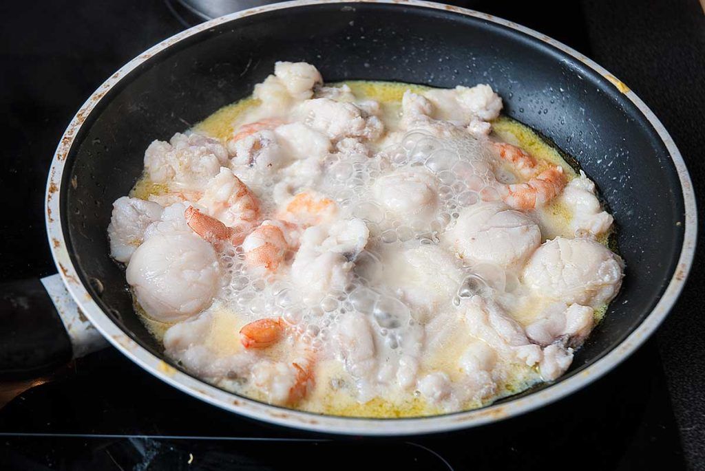 Seafood being quickly fried in a pan releasing their juices.