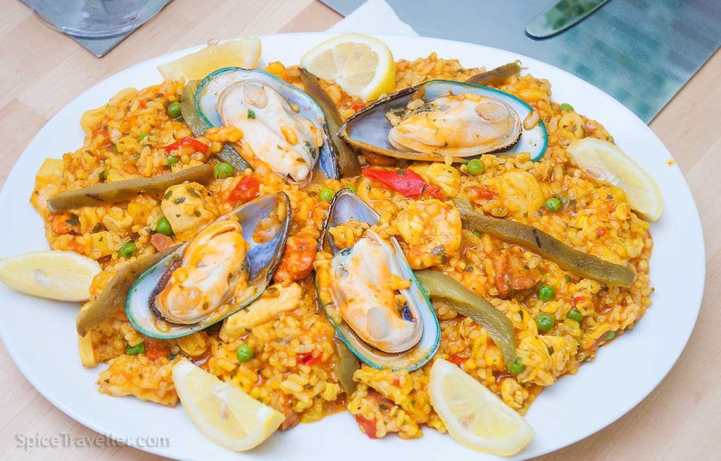 Platter of paella mixta garnished with strips of green roasted peppers, lemon wedges and large New Zealand mussels in their shells.