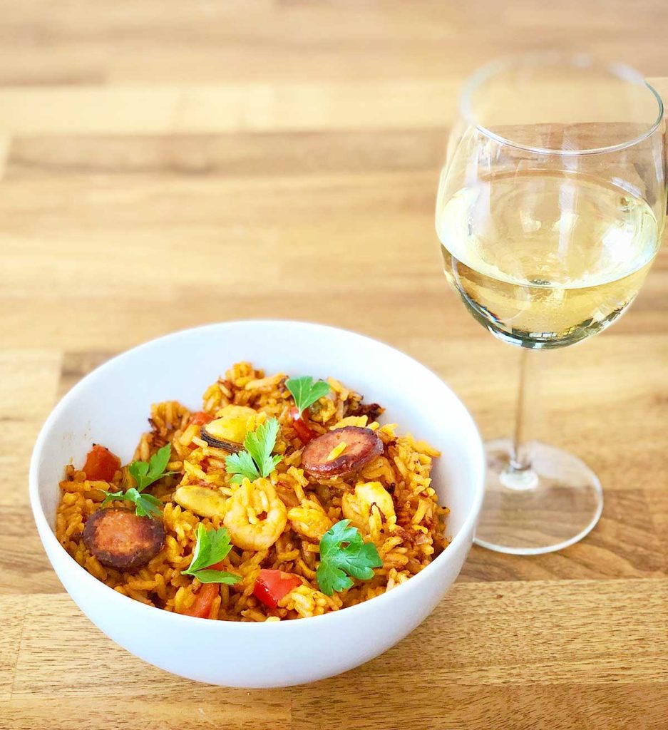 Serving suggestion - bowl of paella mixta served with a glass of white wine.