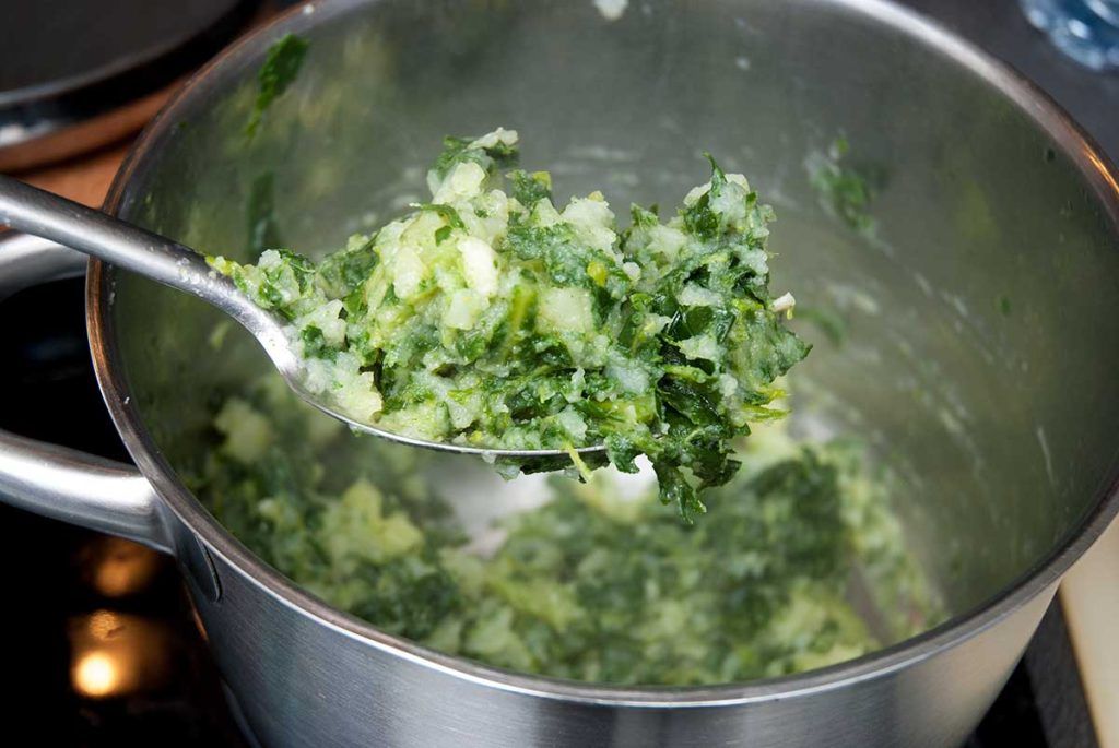 Close-up of a fork holding creamy Croatian chard and potato mash, with the pot of mash blurred in the background.