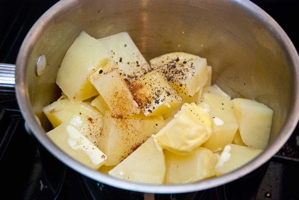 Boiled potato chunks with butter and spices ready to mash.