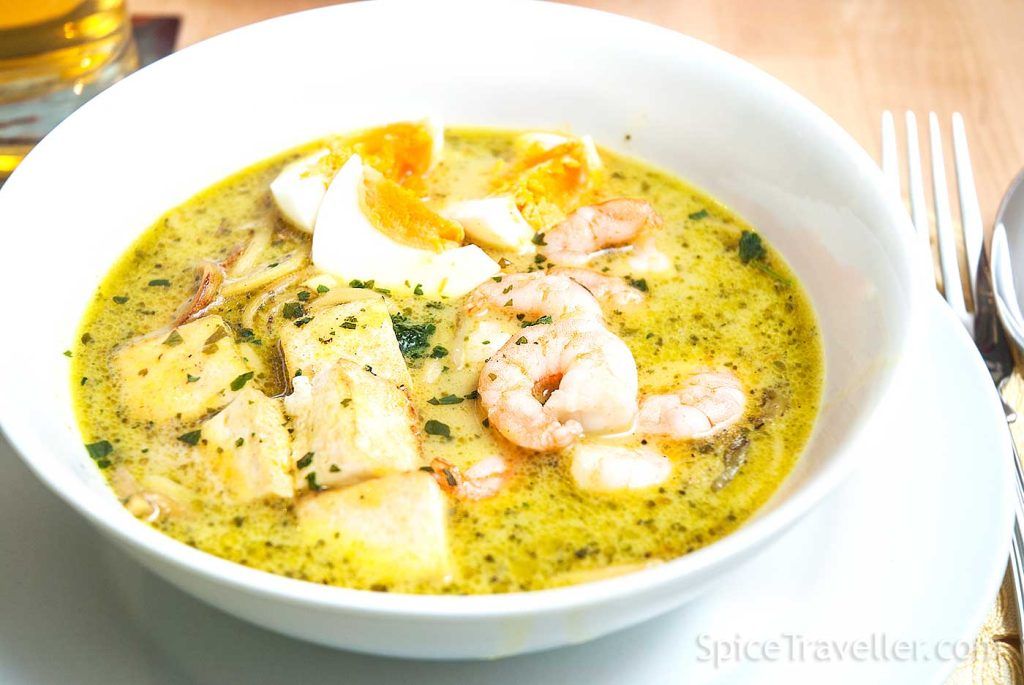 Close up of Malaysian curry laksa with tofu and prawns in a white bowl.