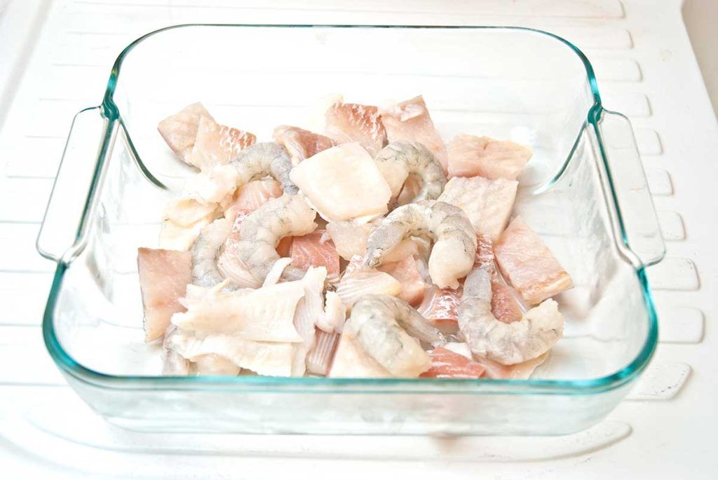 Mixed fish pieces and king prawns layered in baking dish.