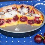 Half of a French custard cake with cherries in the baking dish, showing the soft texture and visible baked-in halved cherries.