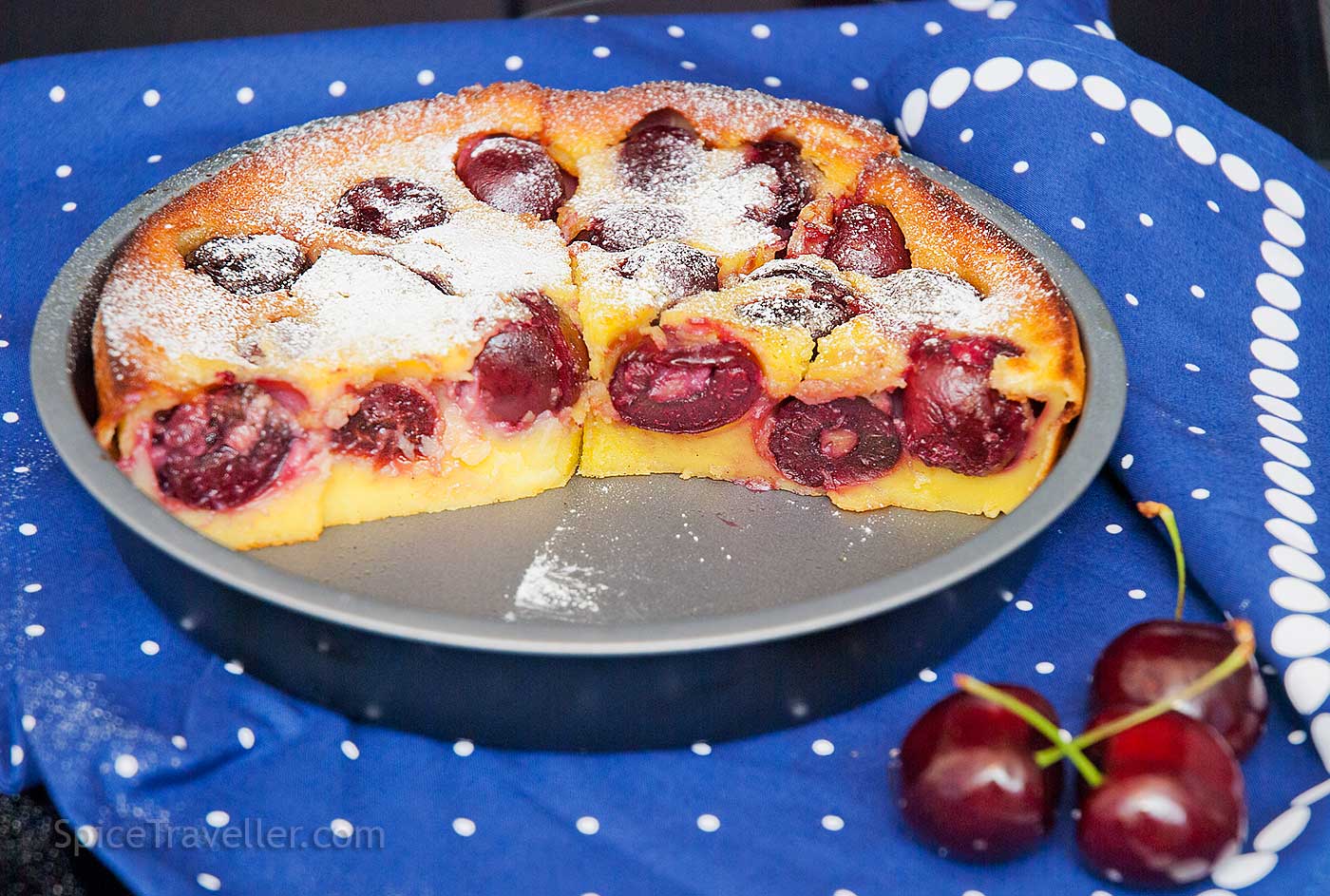 Half of a French custard cake with cherries in the baking dish, showing the soft texture and visible baked-in halved cherries.