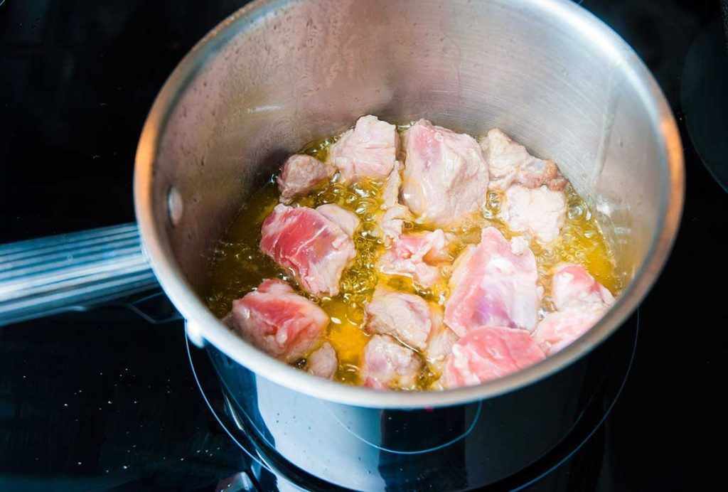 Frying pork pieces in a pot.