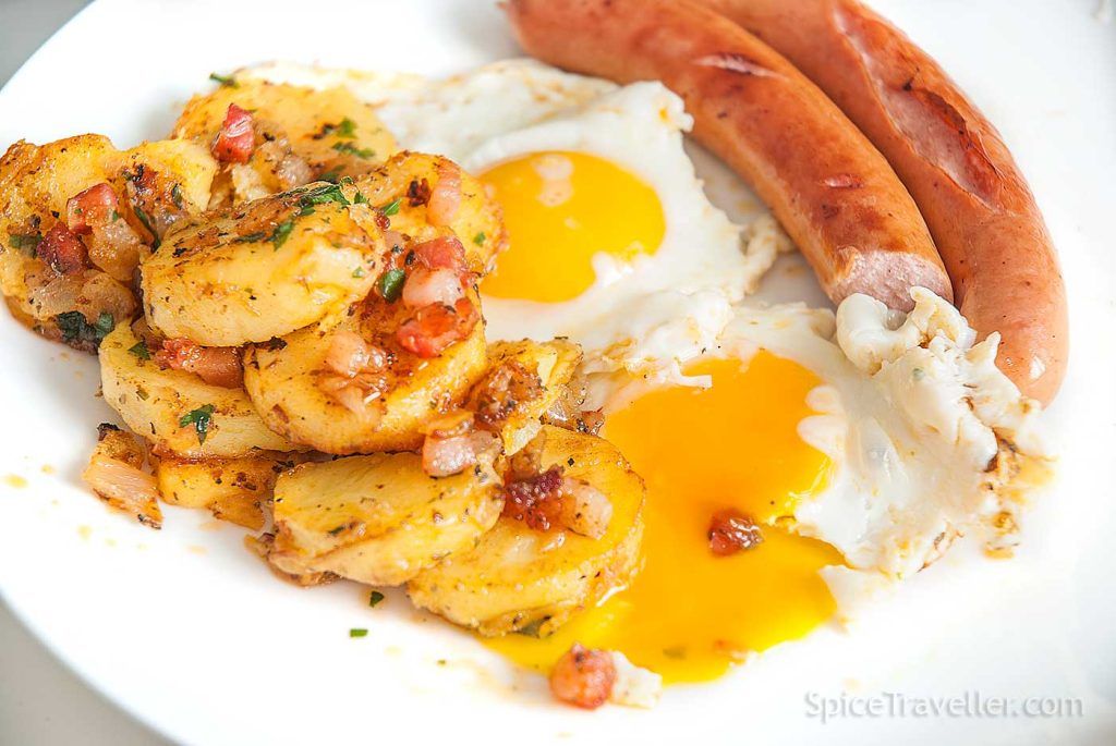 Close up of German fried potatoes (bratkartofflen) served with fried eggs and German Bratwurst.