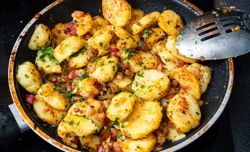 German fried potatoes ready - Fried potato slices mixed with fried onion and bacon together with herbs and spices ready to serve.