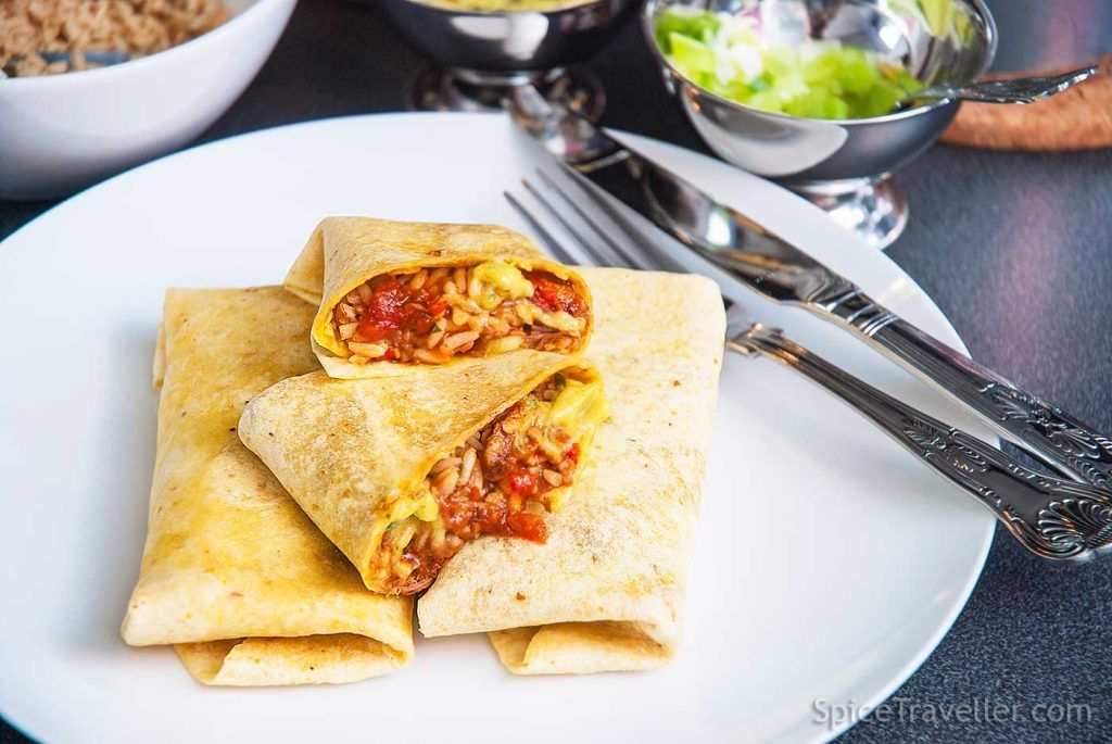 Small thin burritos served elegantly on a plate, cut in half showing the filling.