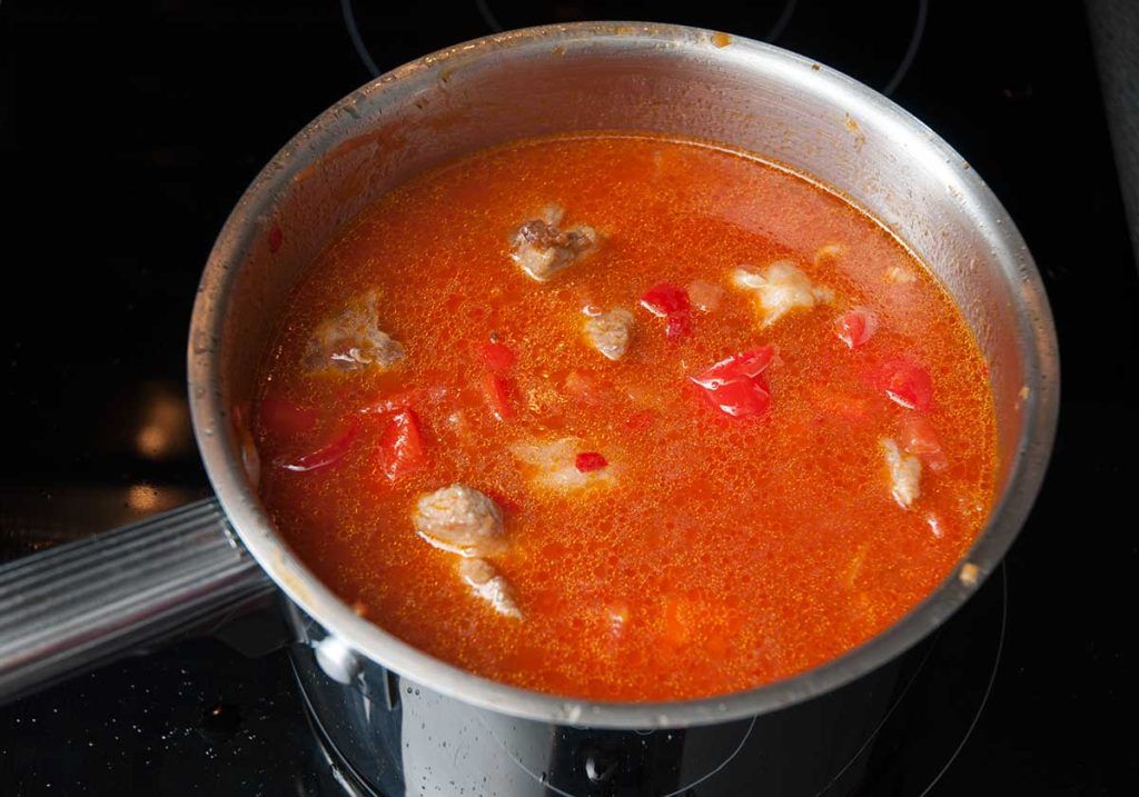 Added chopped tomatoes, fried pork pieces and water to the pot with onions and peppers.