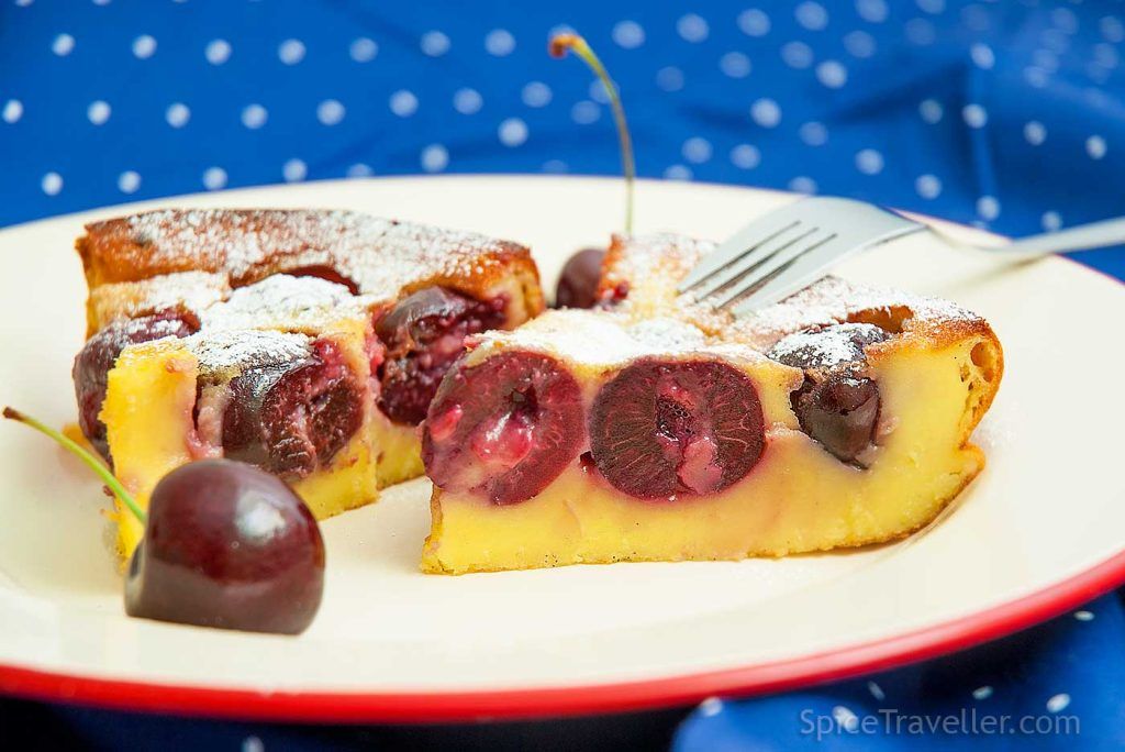 Close-up of a slice of French custard cake with cherries (Clafoutis), showing soft set batter and halved cherries baked into the centre.