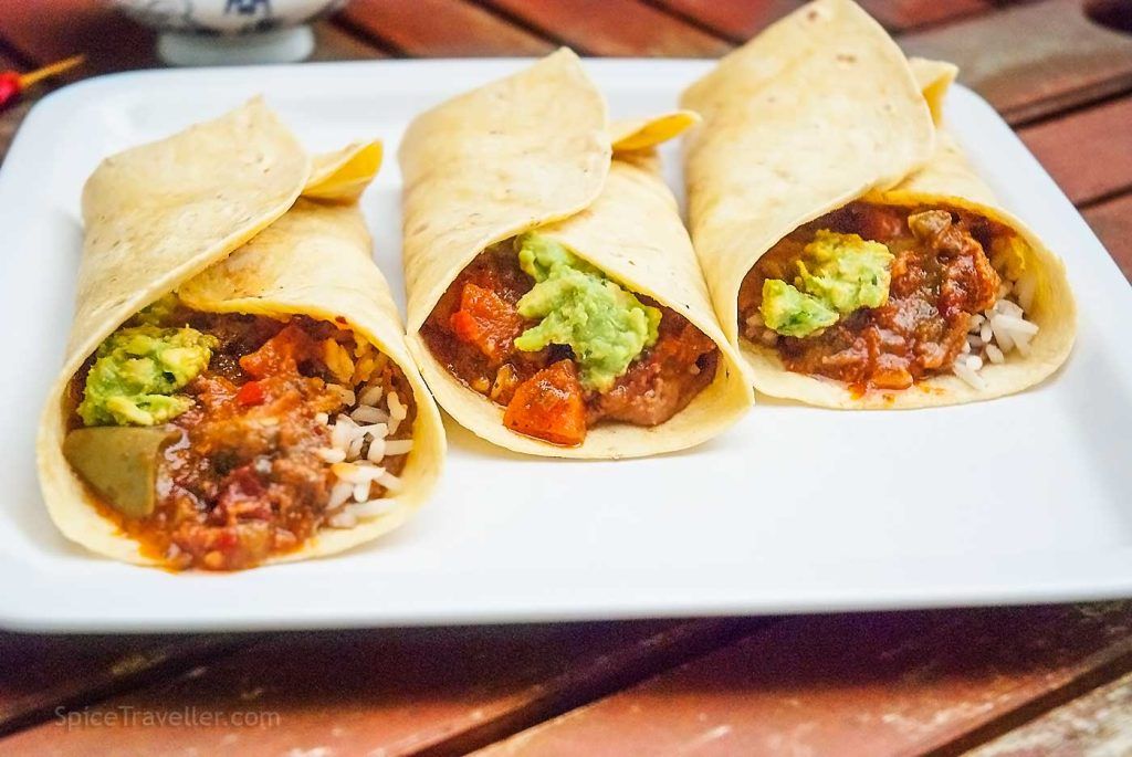 Three tex-mex pork burritos servedon a plate, with one side open, showing the filling.