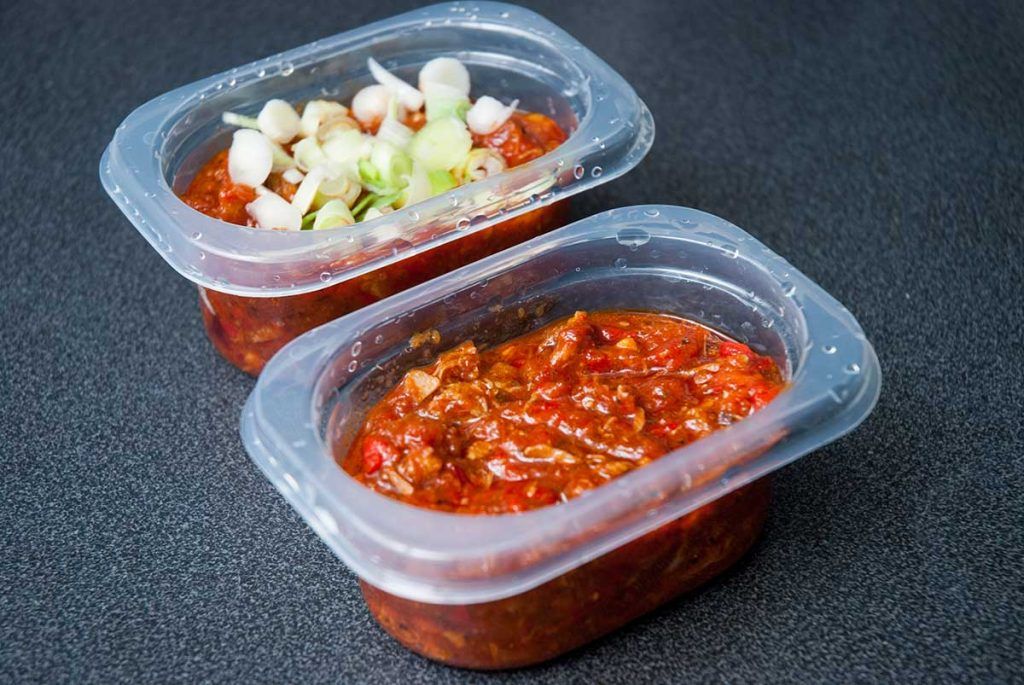 Cooked pork burrito filling portioned into small plastic containers, ready for freezing.