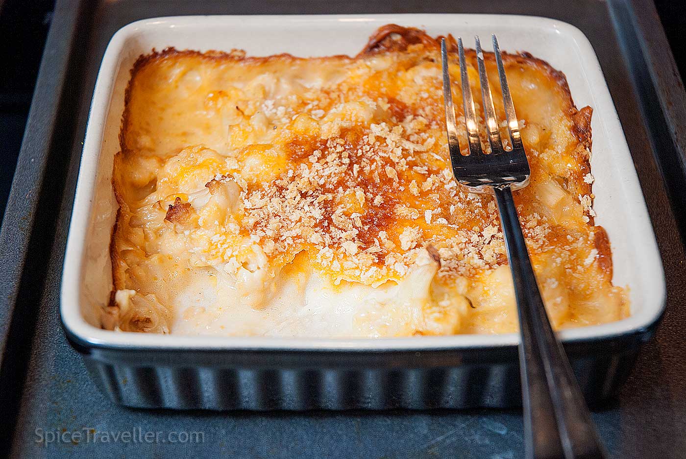 Partially eaten baked cauliflower cheese in a small rectangular dish, with golden topping and visible cauliflower florets in a creamy cheese sauce.