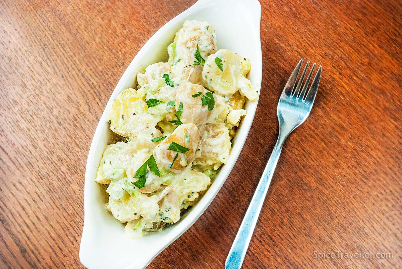Creamy British new potato salad with herbs served in an oval dish.