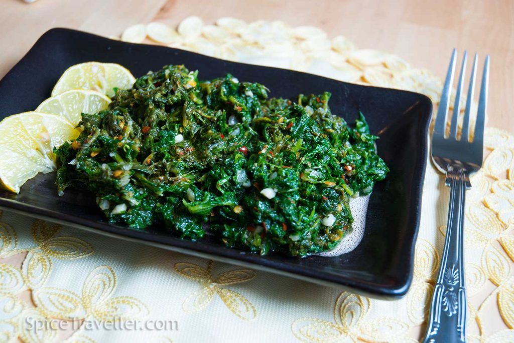 Malaysian spicy spinach and three slices of lime served as a side dish on a small black rectangular plate.