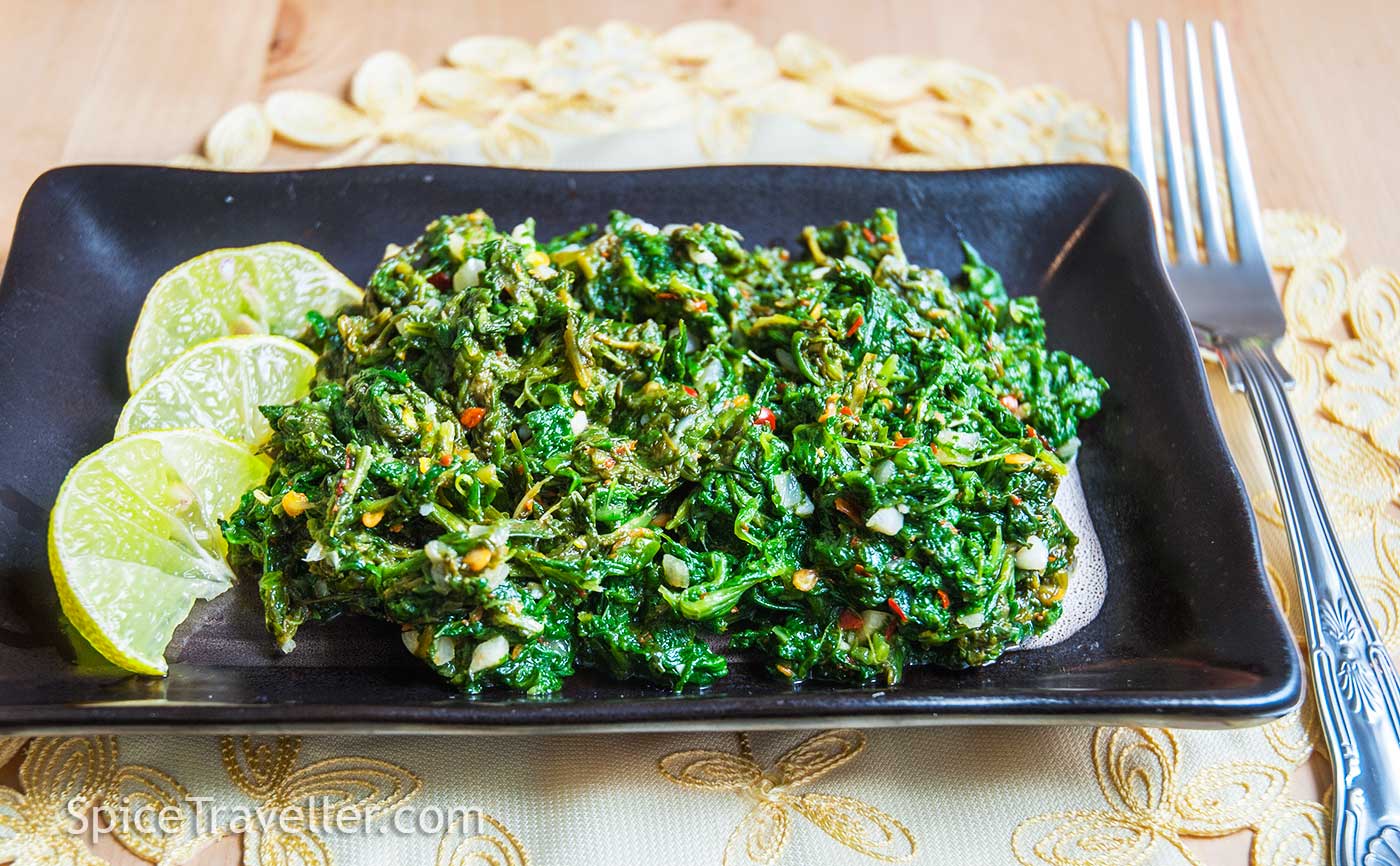 Malaysian spicy spinach served with lime wedges.