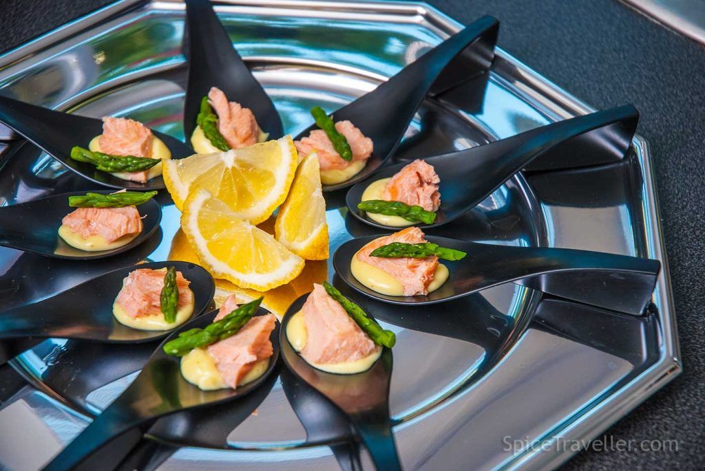Spoon canapés with Hollandaise sauce,, poached salmon and asparagus tips, arranged on a serving tray.