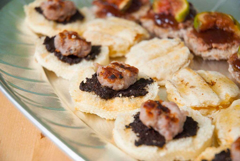 Close up of canapes with black olive spread and grilled sausage slice.