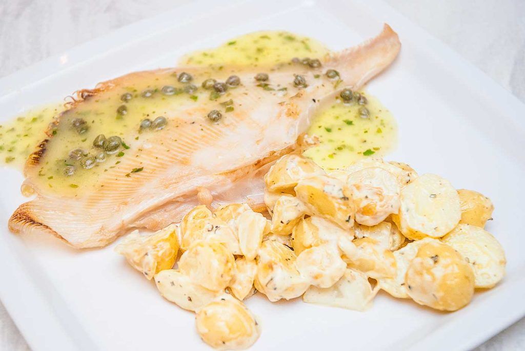 Pan-fried skate topped with caper sauce on a plate with a side of creamy potato salad.