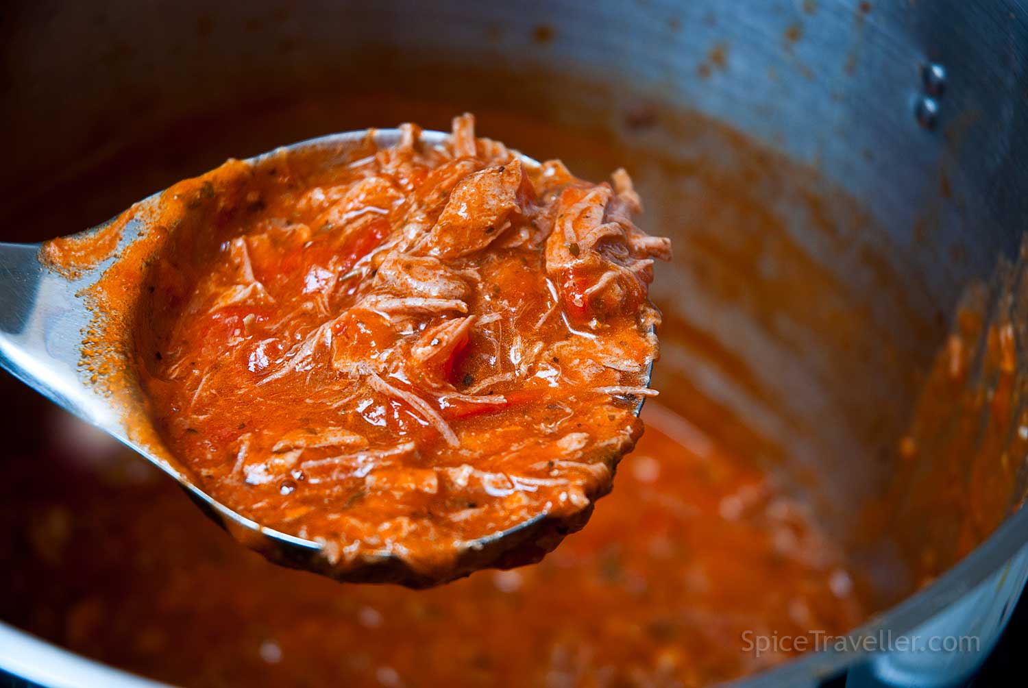 Ladle lifted above the pot, showing a rich, thick pork and tomato sauce in close-up.