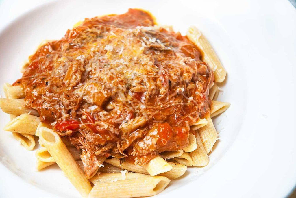 Penne pasta served with a generous amount of pork in tomato sauce spooned over the top.