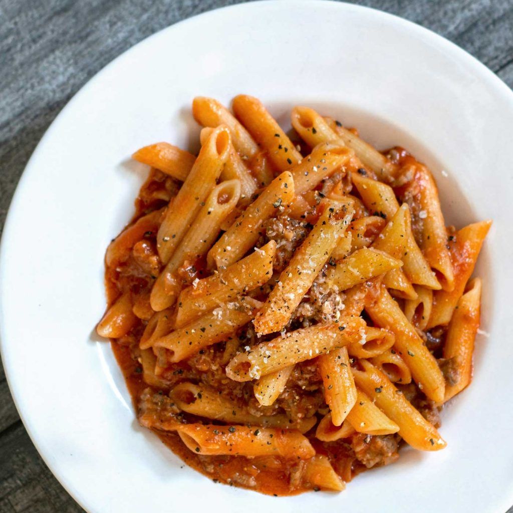 Penne pasta fully mixed with pork and tomato sauce before serving.