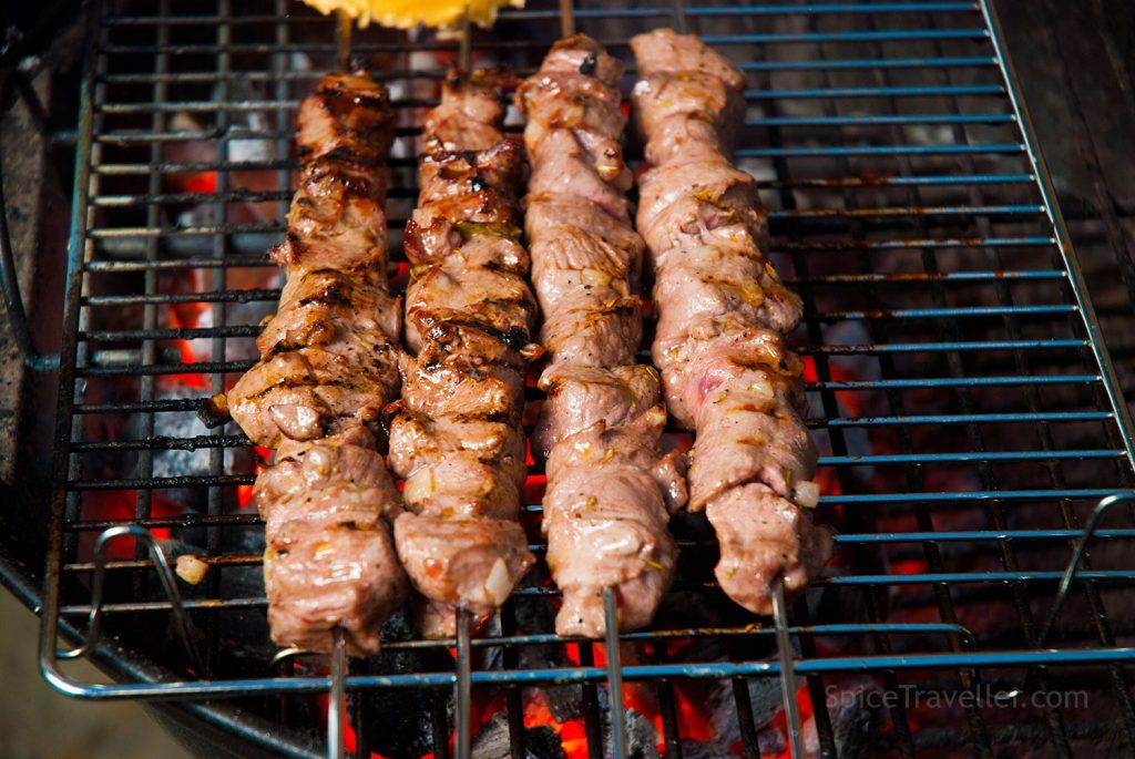 Four skewers of grilled lamb cooked over charcoal, with charred edges and evenly browned, juicy meat.