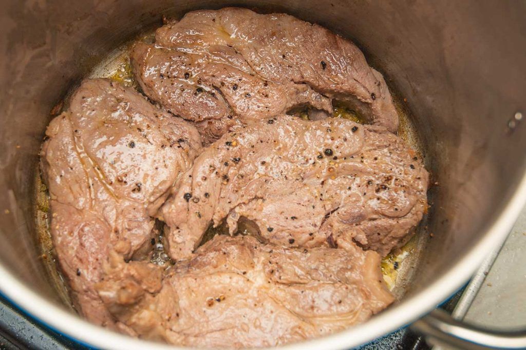 Pork shoulder steaks fully seared in a pot, with browned edges and caramelised surface.