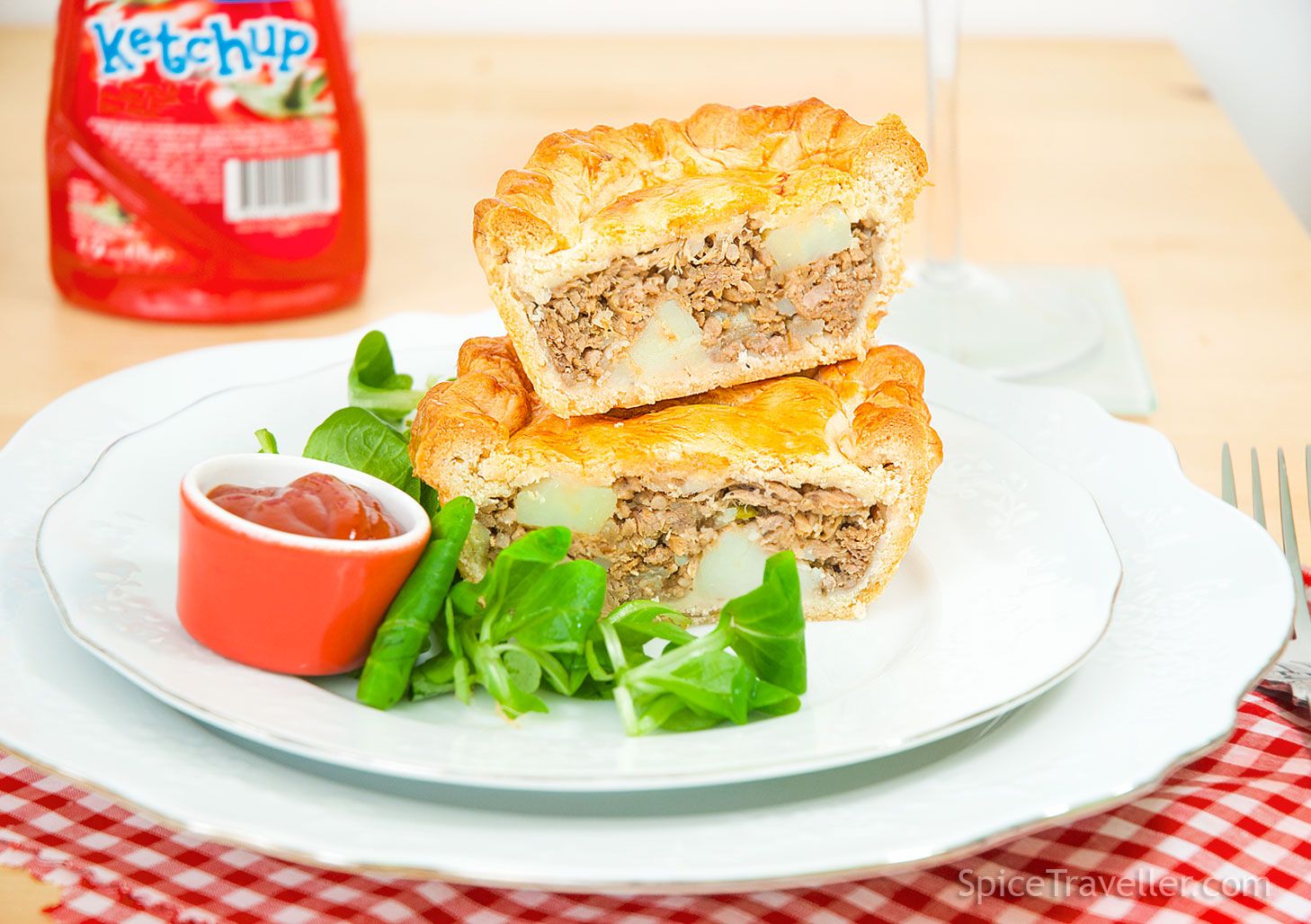Mini Tourtiere meat pie cut in half to show the filling, with visible meat and potato, served with salad and a small tub of ketchup.