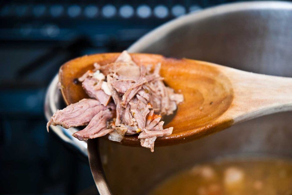 Close-up of tender pork resting on a wooden spoon, showing how it naturally separates into soft segments after slow cooking.