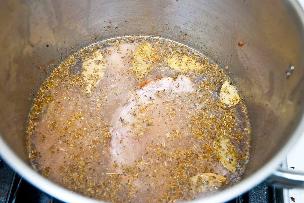 Pork steaks returned to the pot with broth and fresh herbs added, just before slow cooking begins.