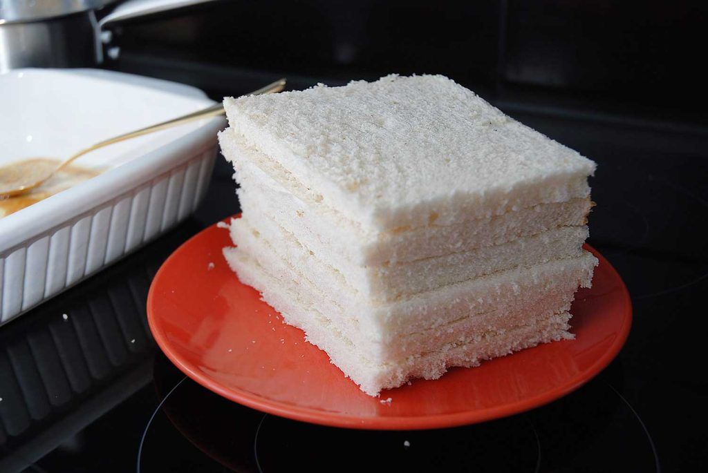 Sliced square white bread without crusts, stacked and ready for pudding.