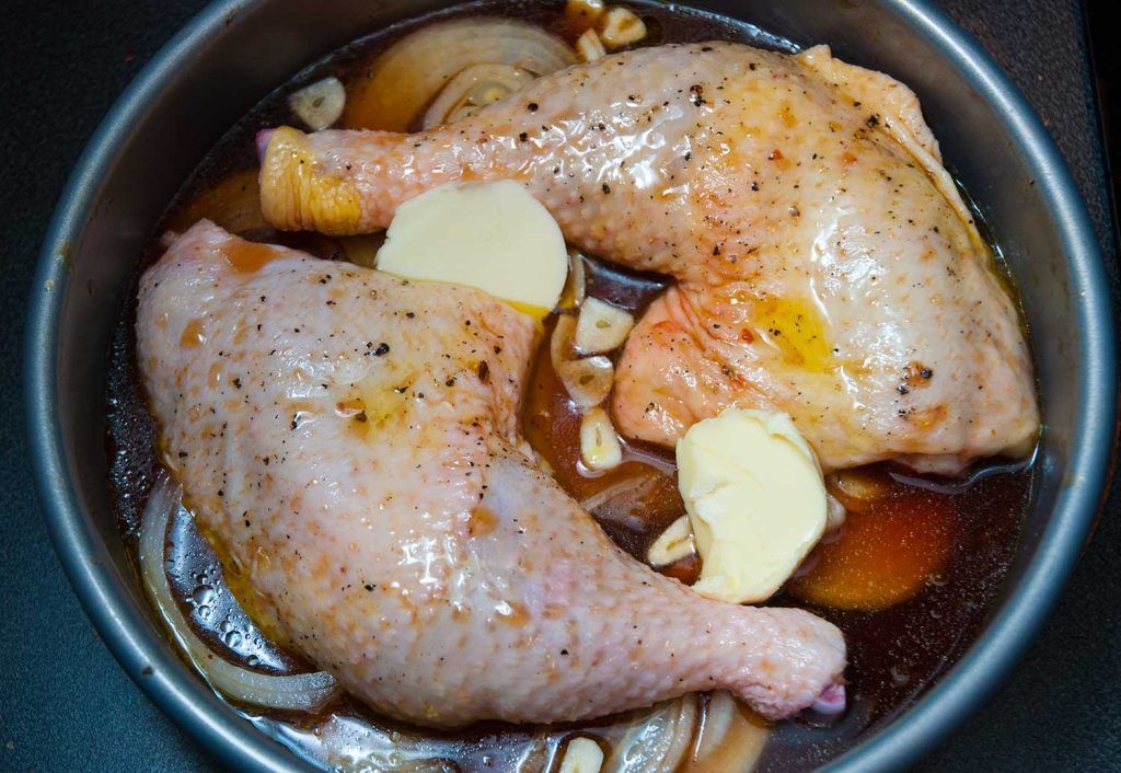 Raw chicken legs in Texas-style BBQ sauce, prepared in a round baking dish before roasting.