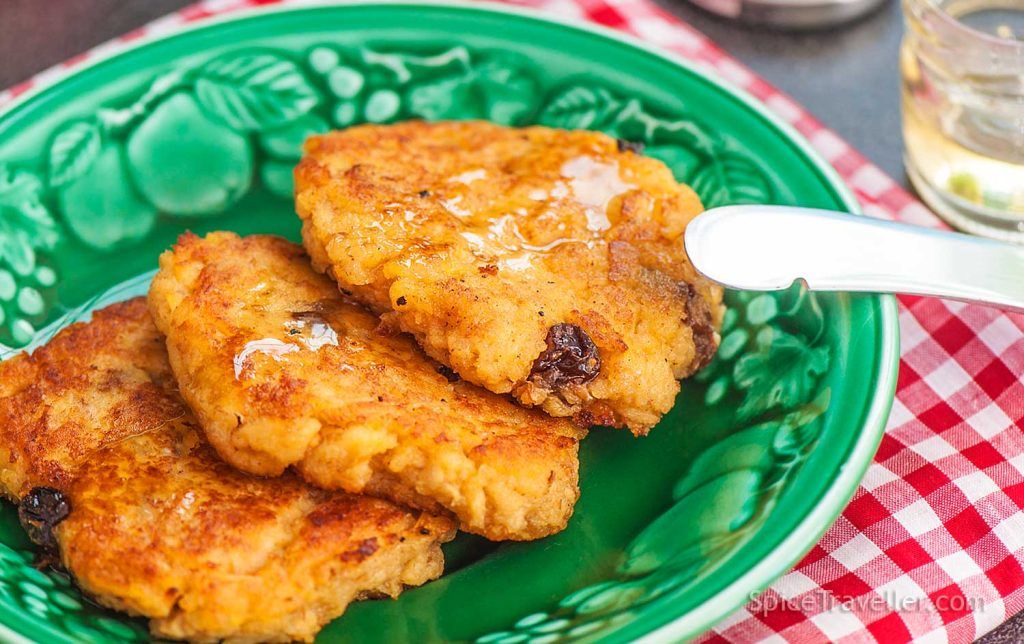 Close up of three Croatian apple fritters on a green plate, drizzled with honey.