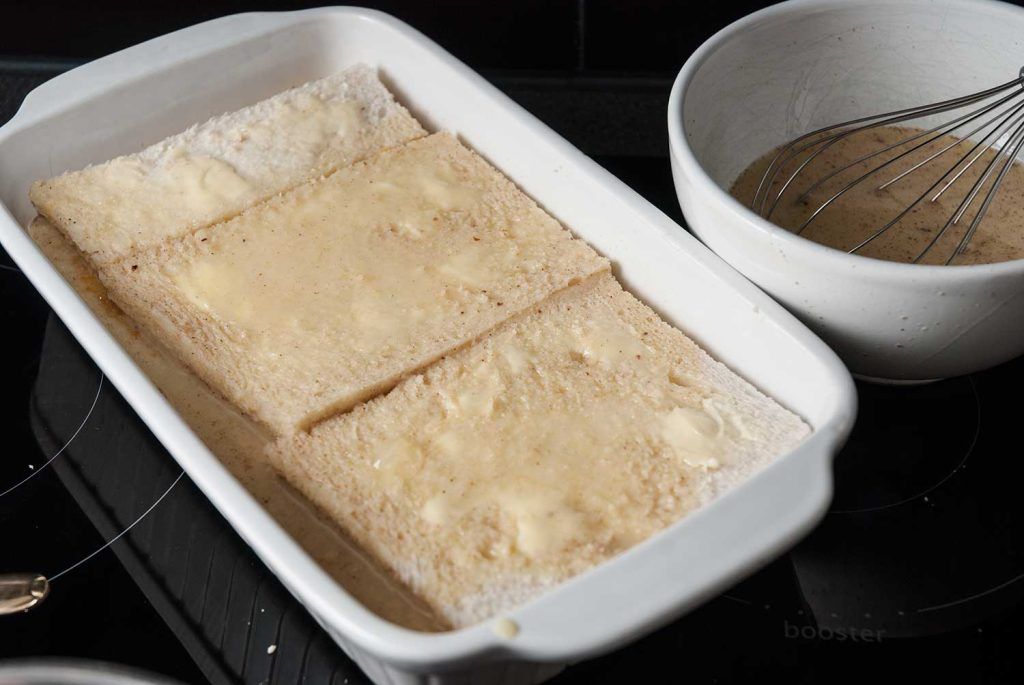 Top layer of buttered bread in the dish with a bowl of egg mixture beside it.