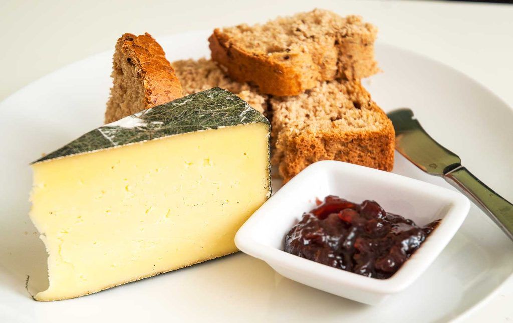 Wedge of cheese with slices of brown bread served with a prune jam in a small dish.