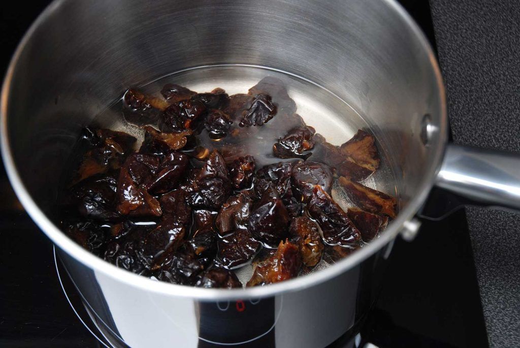 Pitted prunes soaking in hot water in a saucepan.