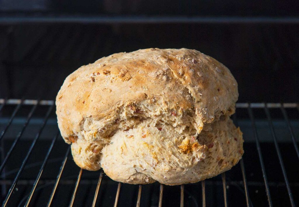 Freshly baked Aussie damper loaf with beer and bacon cooling on a wire rack.