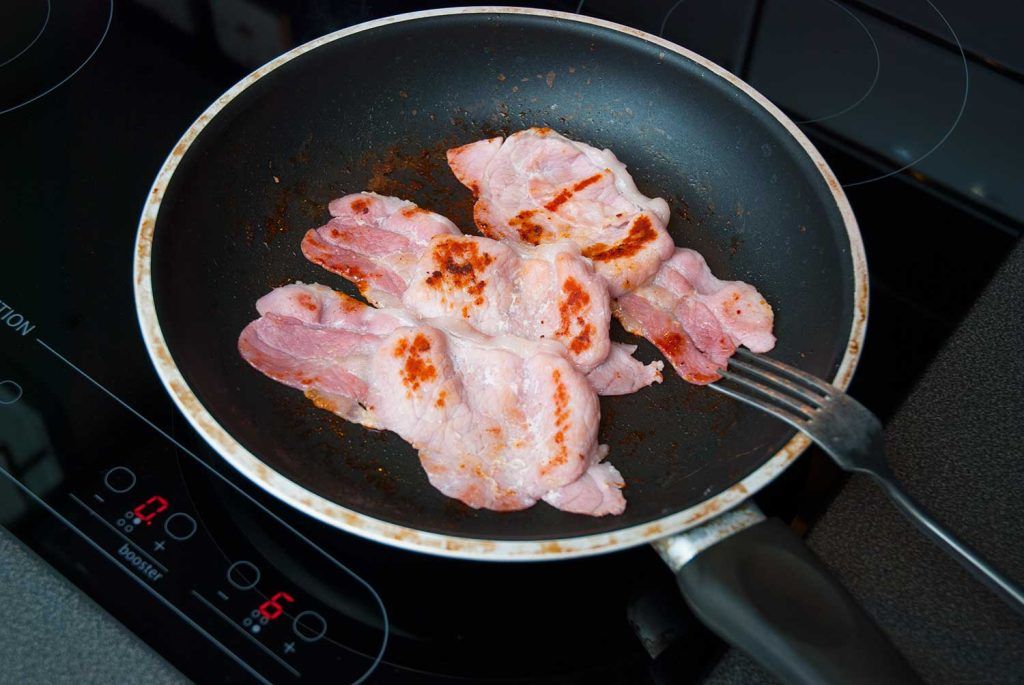 Bacon frying in a dry pan until golden and crisp for damper bread.