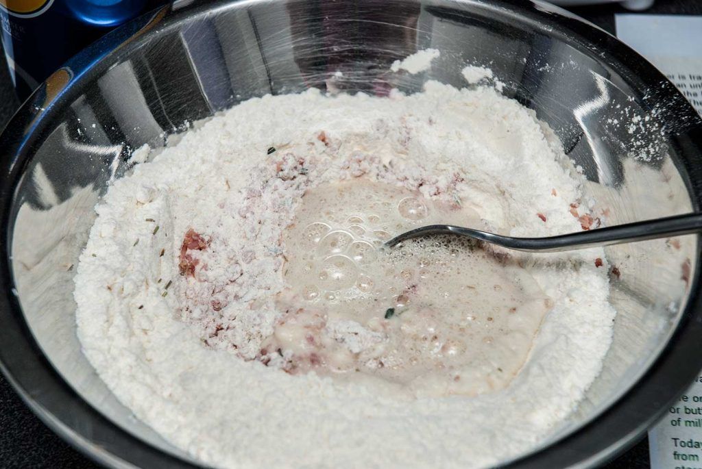 Light beer poured into flour, bacon, and rosemary mixture to make damper dough.